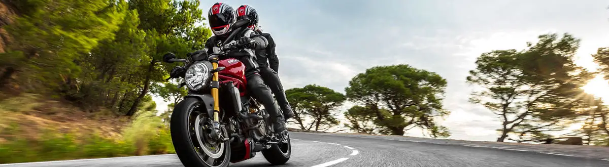 two guys riding a red bike on a roadway at full speed on kindof clear gray sky